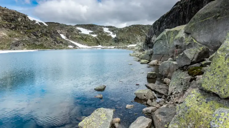 Langvatbet am Hardangerjokulen Langvatnet mit felsigem Auferbereich. Der Wanderweg führt immer entlang der Felsen auf Trittsteinen am Ufer entlang.