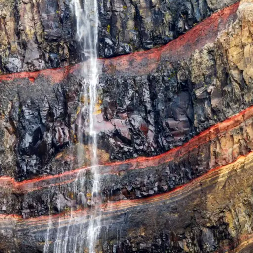 Geologische Schichten am Hengifoss Wasserfall Detailaufnahme des Hengifoss Wasserfalls mit markanten roten Tonschichten zwischen dunklem Basaltgestein.