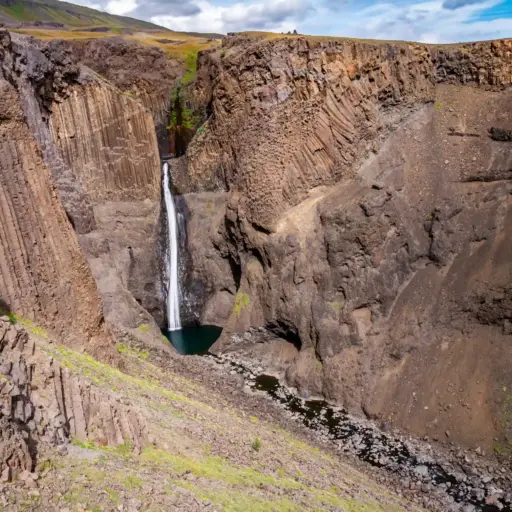 Litlanesfoss Wasserfall mit Basaltsäulen Der Litlanesfoss Wasserfall in Island, umgeben von hohen, vertikalen Basaltsäulen in einer tiefen Schlucht.