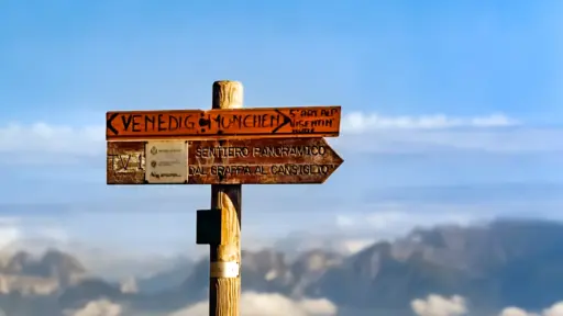 Holzwegweiser für den Traumpfad mit dem Schriftzug "München-Venedig" mit Bergen der Alpen im Hintergrund