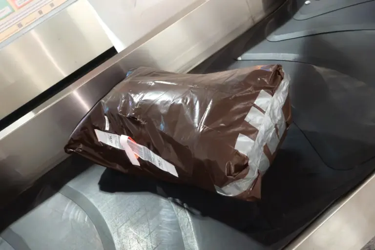 Rucksack in braunem Schwerlast-Müllsack, eng getapet, mit Gepäcklabel auf Gepäckband