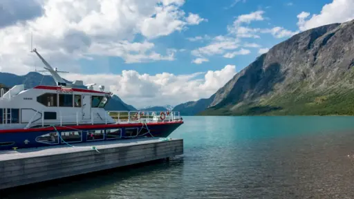 Die Fähre Gjendine am Anleger Gjendesheim Das rot-blaue Schiff Gjendine am Holzsteg des smaragdgrünen Gjendesees vor den Bergen von Jotunheimen.