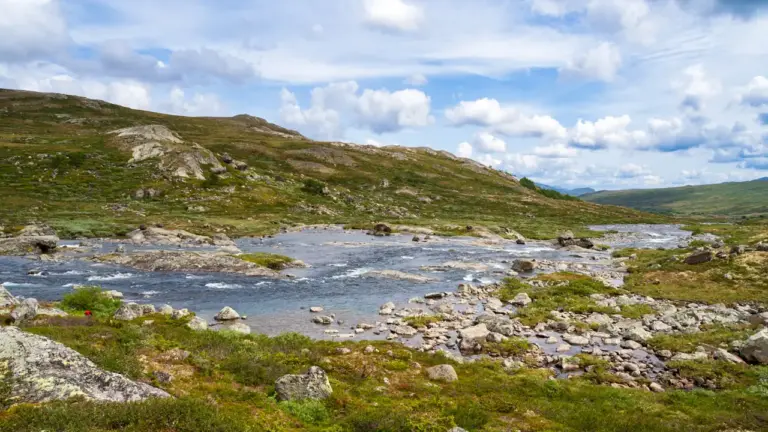 Fluss Russa im Jotunheimen-Nationalpark in Norwegen, ein winziger Wanderer in roter Regenjacke zeigt die Größe der Landschaft.