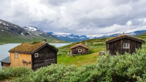 Russvassbu-Hütten am Russvatnet mit Blick auf den Surtningssue Hütten von Russvassbu am Russvatnet mit Blick auf die wolkenverhangenen, teils schneebedeckten Berge des Surtningssue im Jotunheimen-Nationalpark.