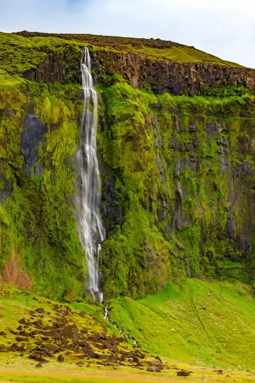 Drífandi í Fljótshlíð dei Schleier des schmalen Wasserfalls Drífandi über die saftig grüne Felswand
