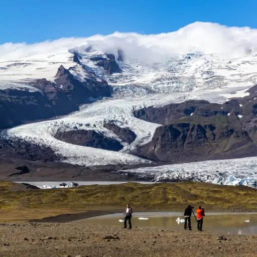 Svínafellsjökull Gletscherzunge – Fotospot an der Ringstraße Fotografen stehen vor der gewaltigen Gletscherzunge des Svínafellsjökull in Island unter einem wolkenverhangenen Gipfel.