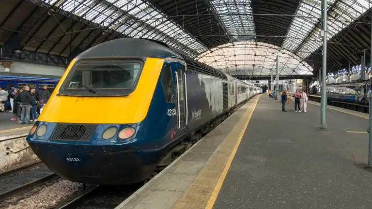Scotrail-Zug am Bahnhof Glasgow Queen Street Ein gelb-grauer Zug im Bahnhof unter einem breiten und lichtem Glasgewölbe.